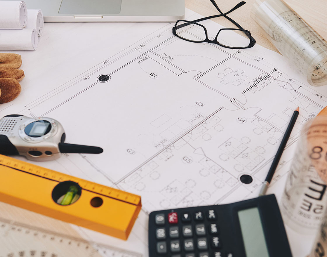Rolled construction drawings, a calculator and a hard hat on a workbench